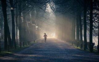 person running near street between tall trees